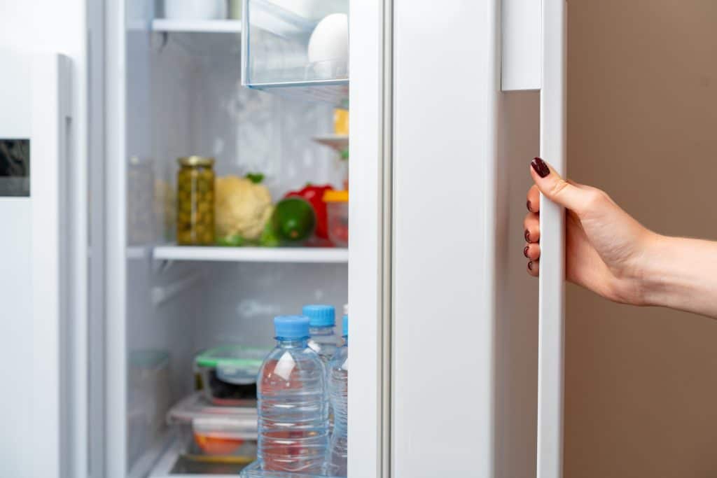 Female hand opens door of a fridge close up