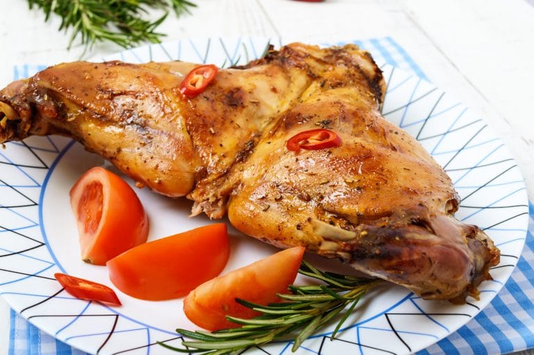 Baked rabbit legs on a plate on a white wooden background.Baked rabbit legs on a plate on a white wooden background.