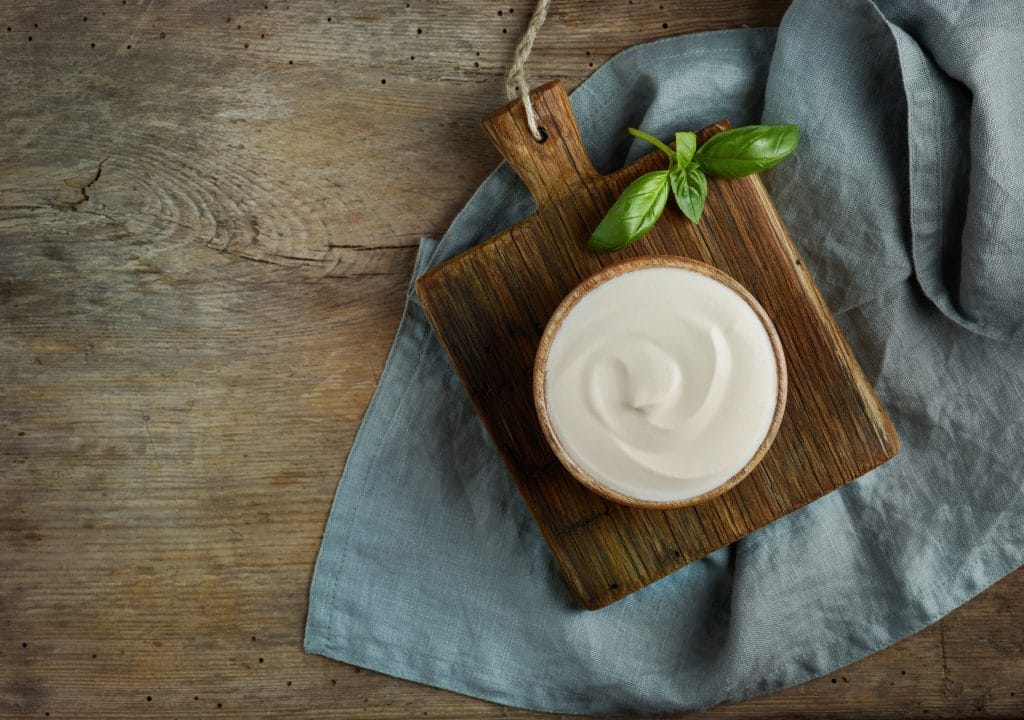 bowl of sour cream on old wooden kitchen table, top view