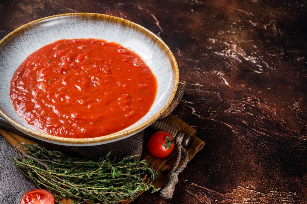 Homemade tomato Passata in rustic plate with herbs. Dark background. Top view. Copy space.
