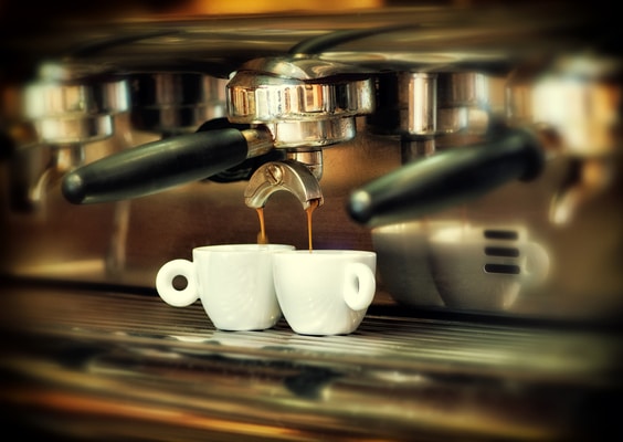 Coffee maker with black handle pours hot coffee into two white ceramic cups. Close-up viewed from the side